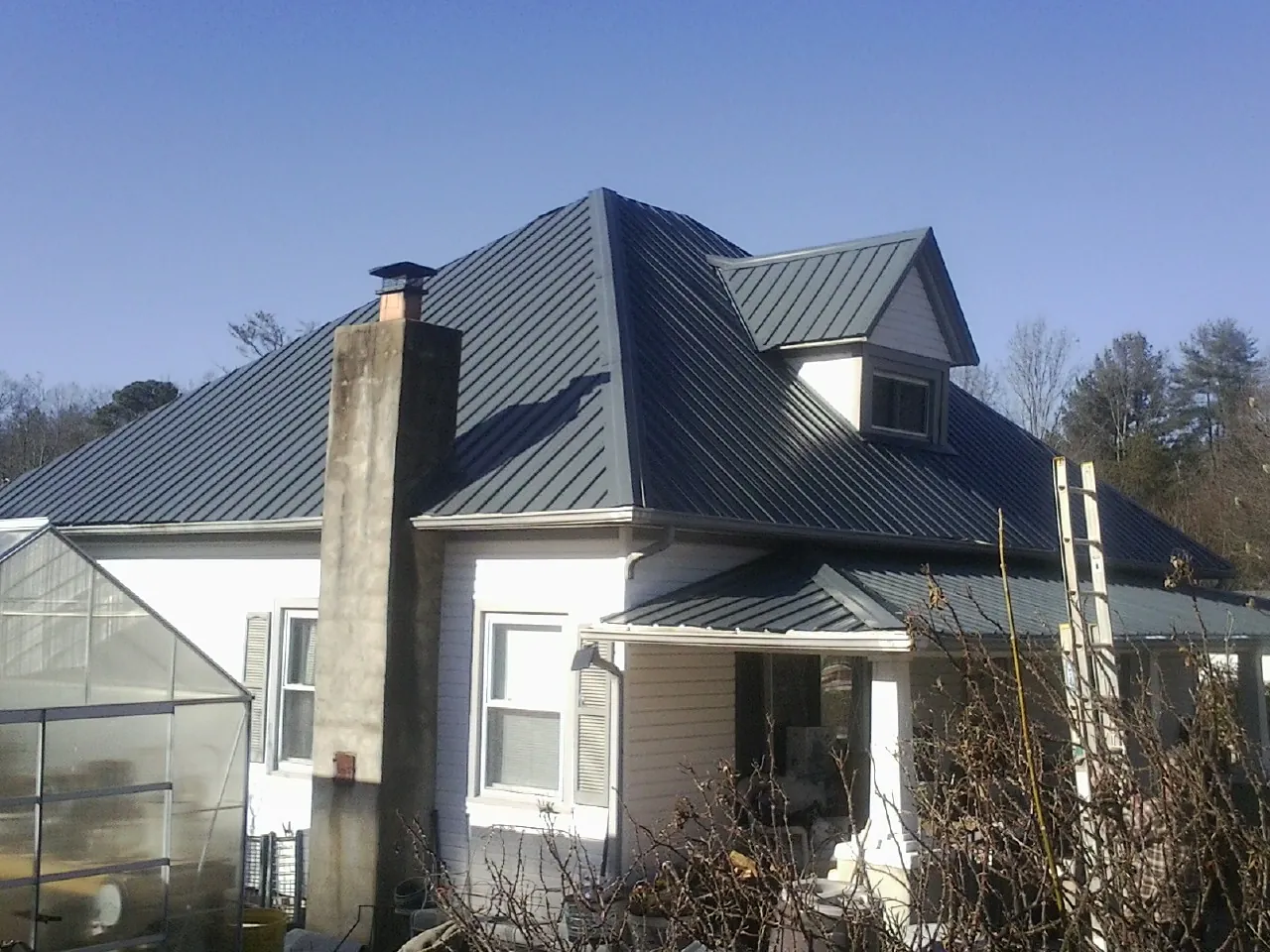 Dark blue standing seam metal roof on a white farmhouse with dormer — Slate & Tile Roof Repair by Roofing Brothers in North Chili