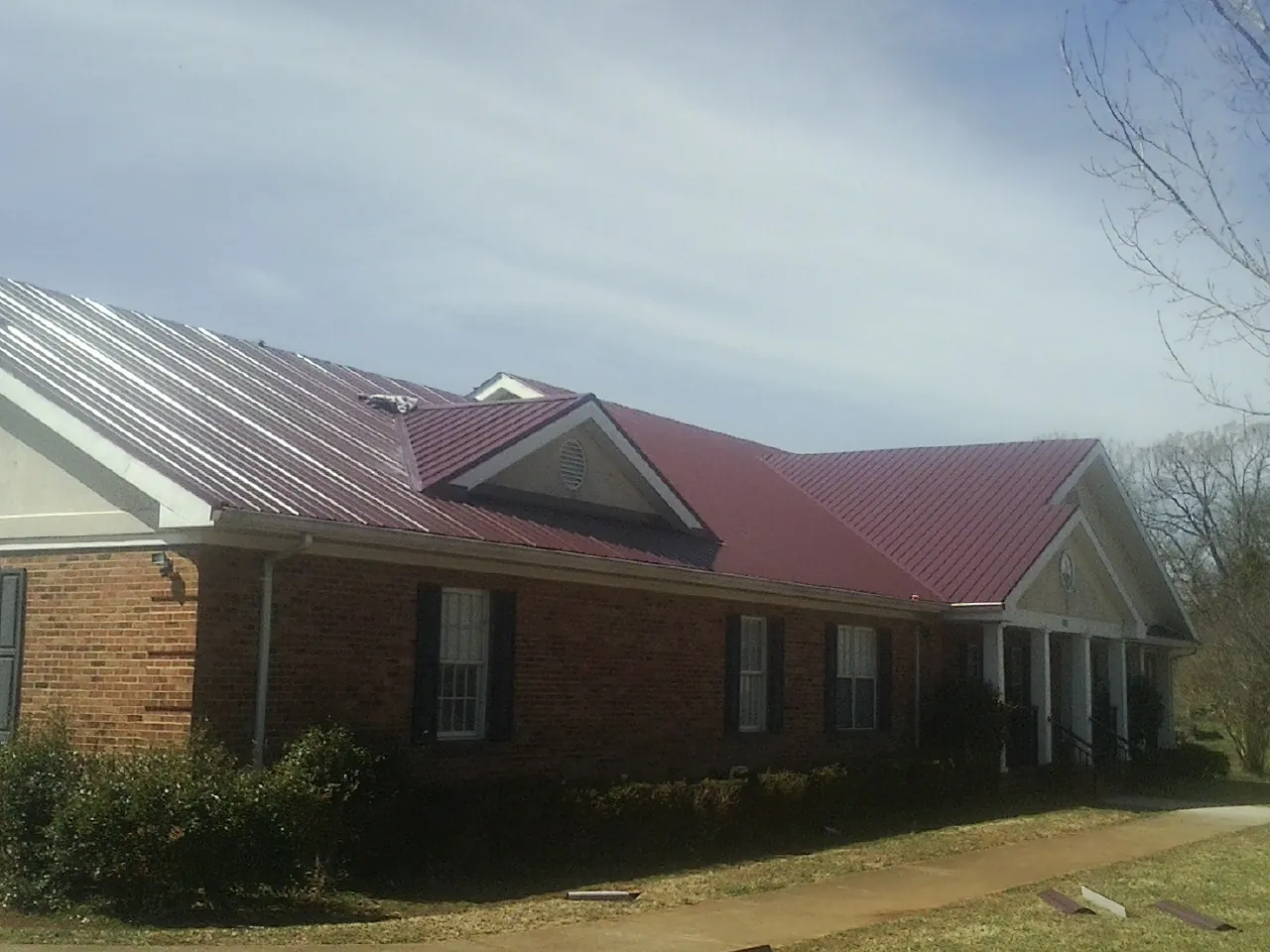 Red metal roof with gabled entries on a long brick building, from a Hail Damage Roof Repair job in North Chili