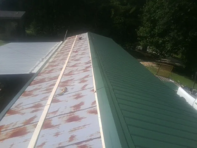 Old rusted panels beside newly installed green metal roofing — Wind Damage Roof Repair by Roofing Brothers in North Chili