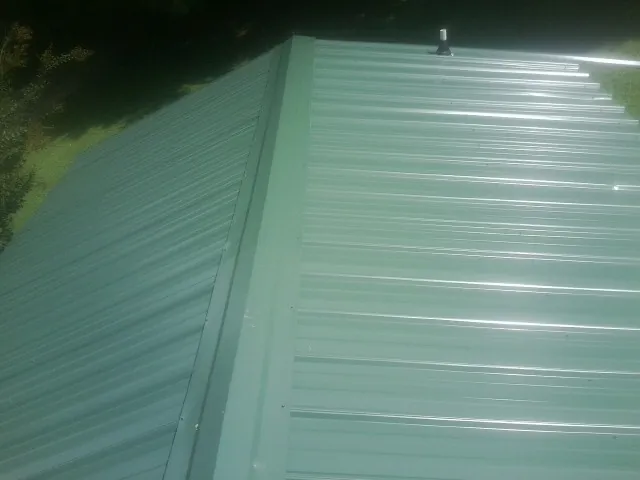New green metal panels meeting at the ridge of a roof — Flat Roof Repair work by our crew in North Chili