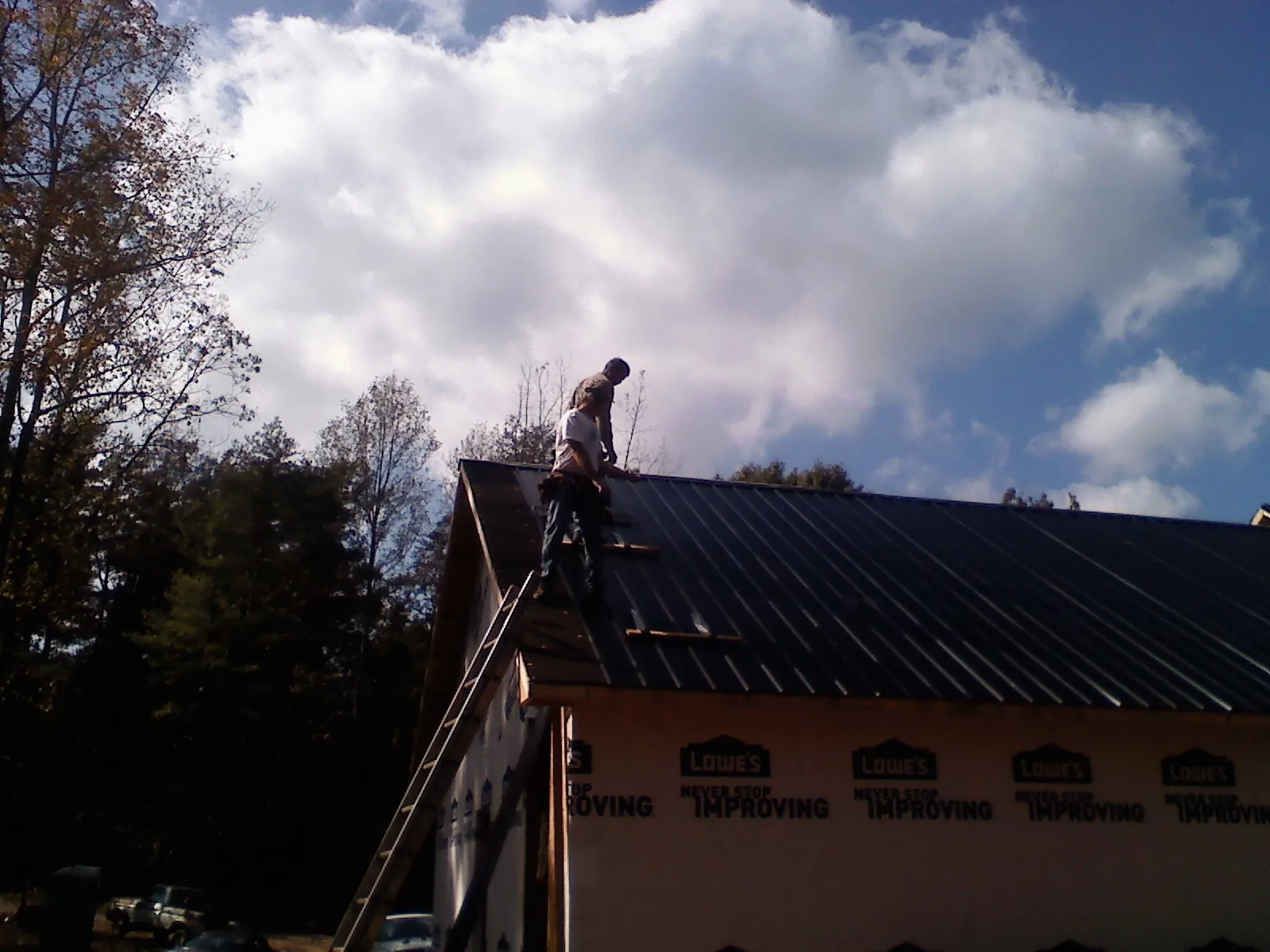 Roofer fastening dark metal panels high against a cloudy sky, from a Roof Inspection job in North Chili