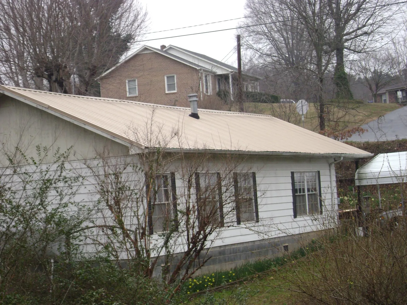 Tan metal roof on a white sided house set into a hillside — Commercial Roofing by Roofing Brothers in North Chili