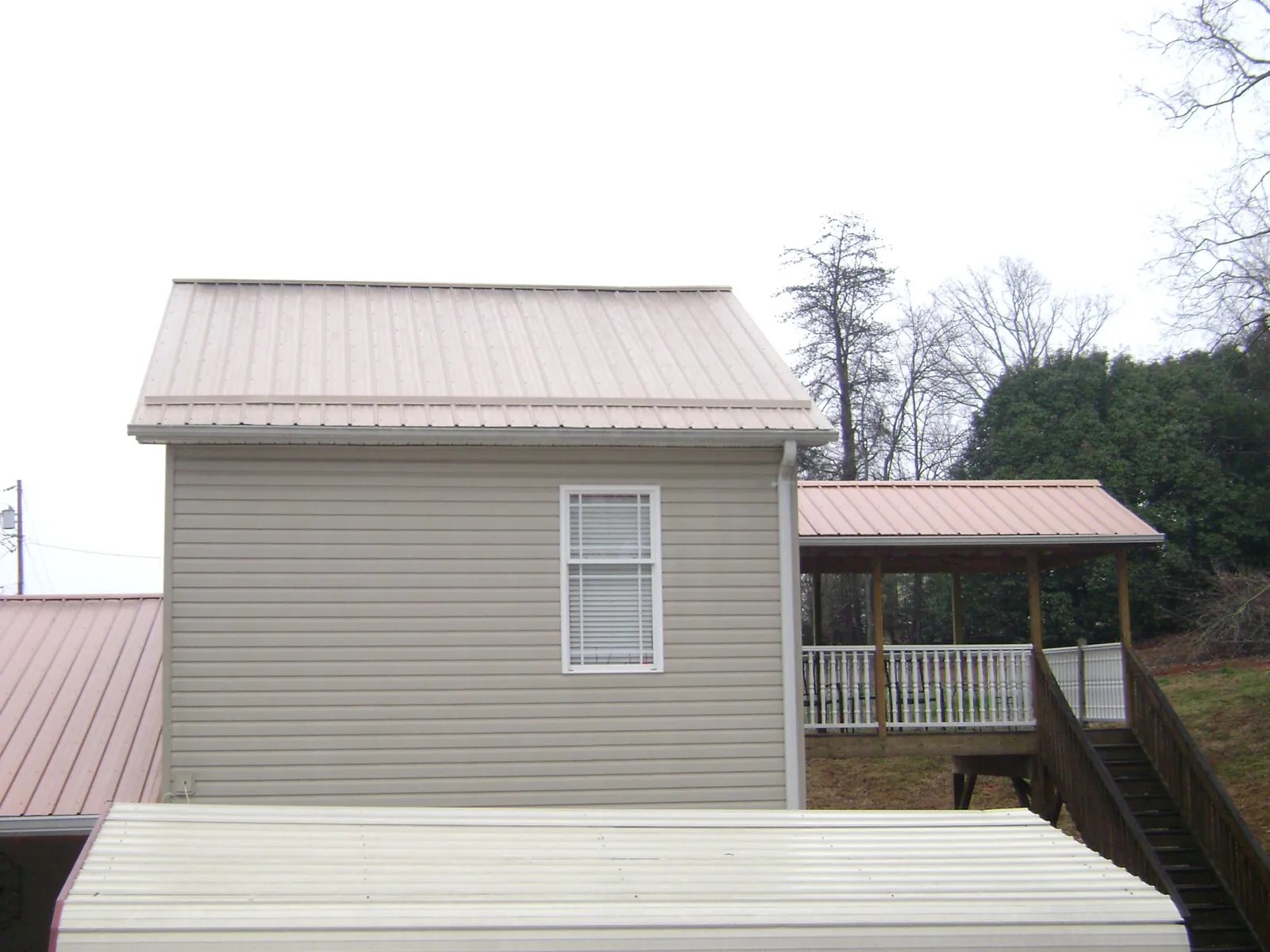 Tan metal roofs on a two story addition and attached porch, from a Roof Replacement job in North Chili
